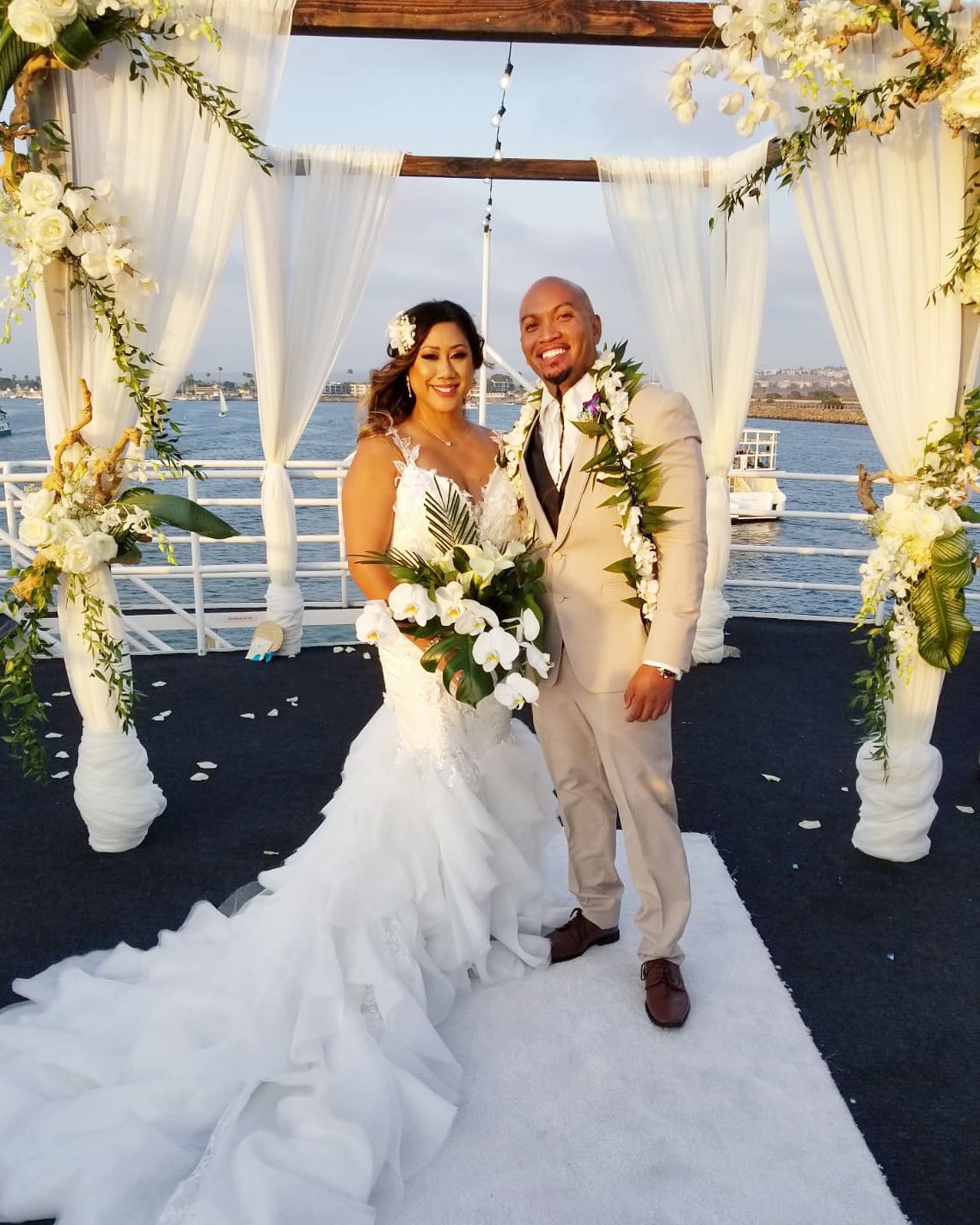 Waterfront wedding ceremony with the newlyweds beneath a draped floral arch