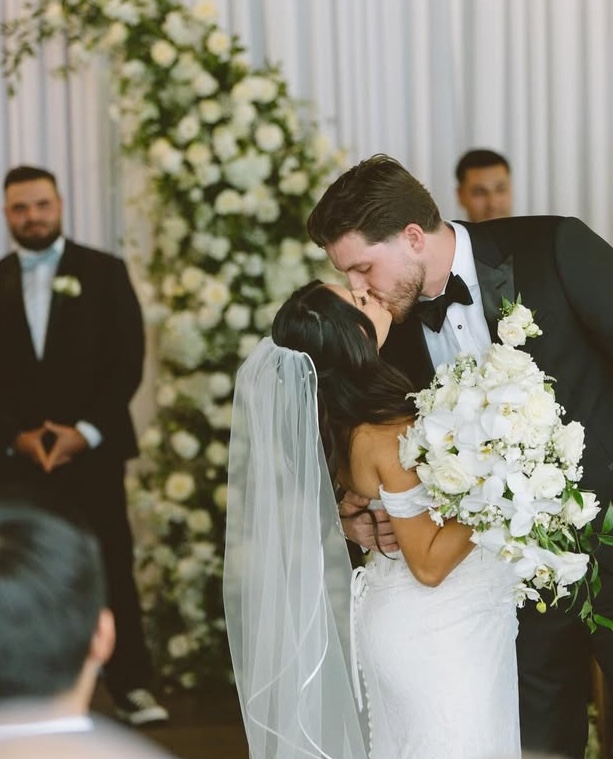 Bride and groom's first kiss framed by a white floral wall