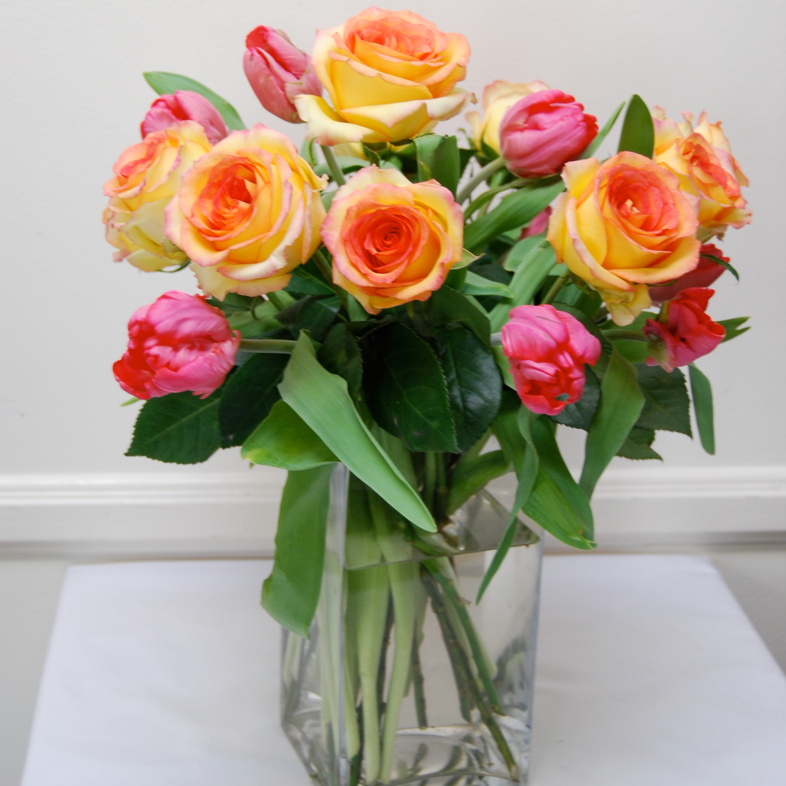 Peach roses and coral tulips garden bouquet in a glass vase